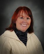 Headshot of Ann Wake wearing a black striped turtleneck and cream zip up sweater.